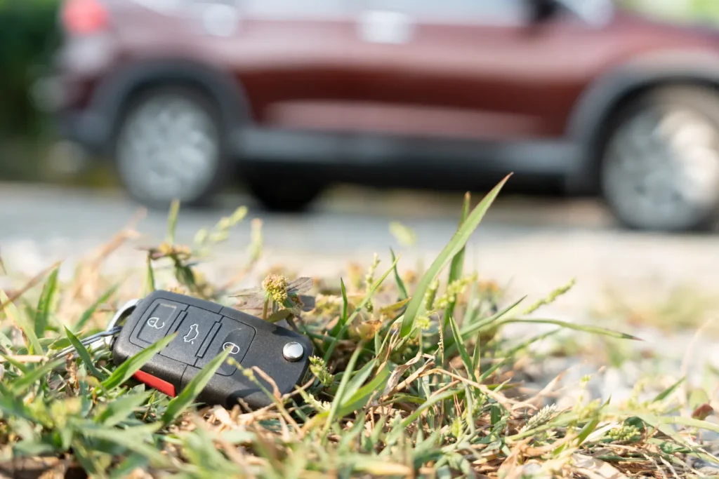 Car key fob lying on grass near a parked vehicle, illustrating vehicle lockout situations handled by Lion Locksmith, an auto locksmith near Silver Spring MD.